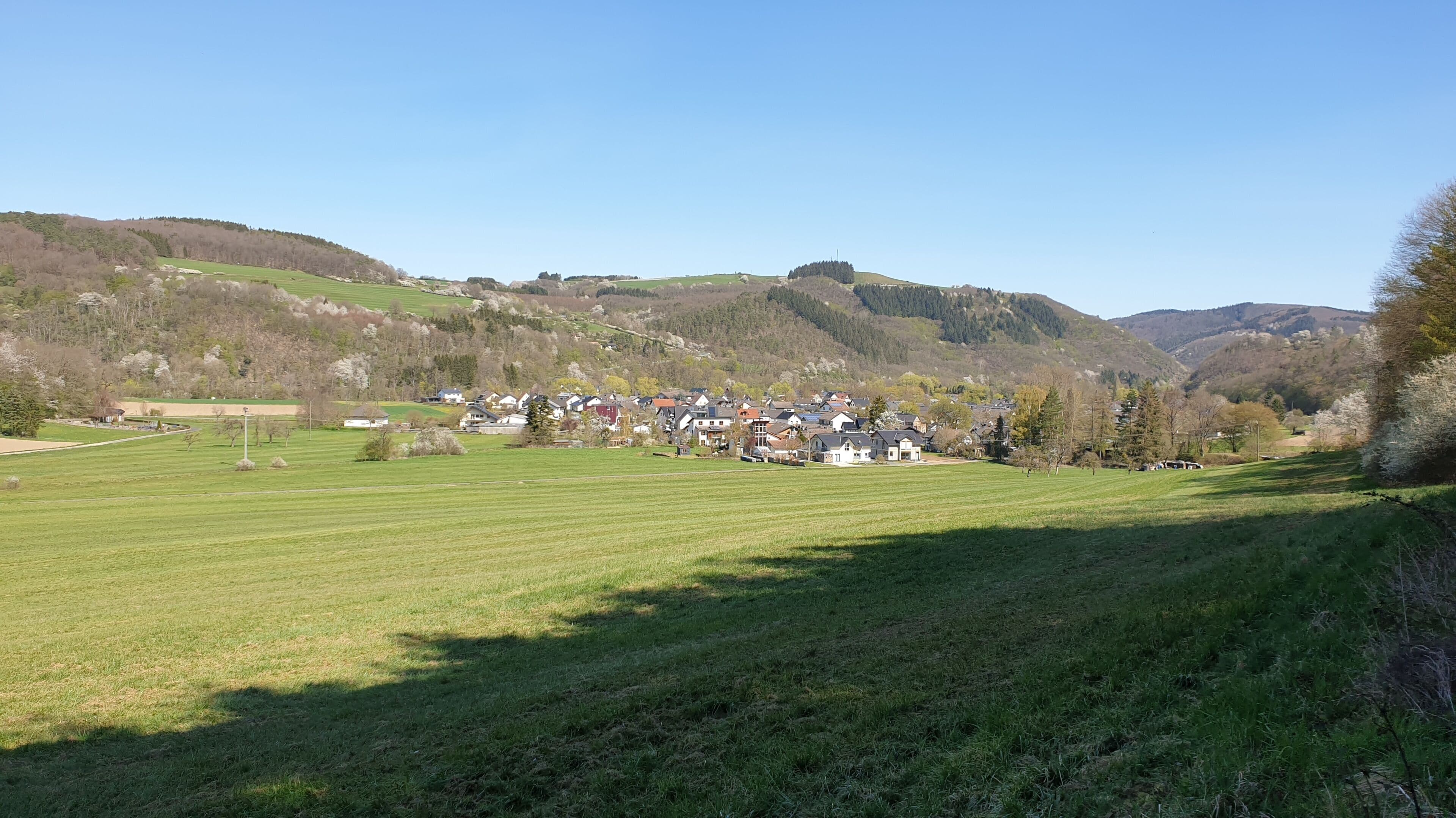 Un pueblo rural con casas, campos abiertos y colinas al fondo.