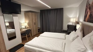 A modern hotel room with a large bed, a desk, a chair, a TV, and a wardrobe.