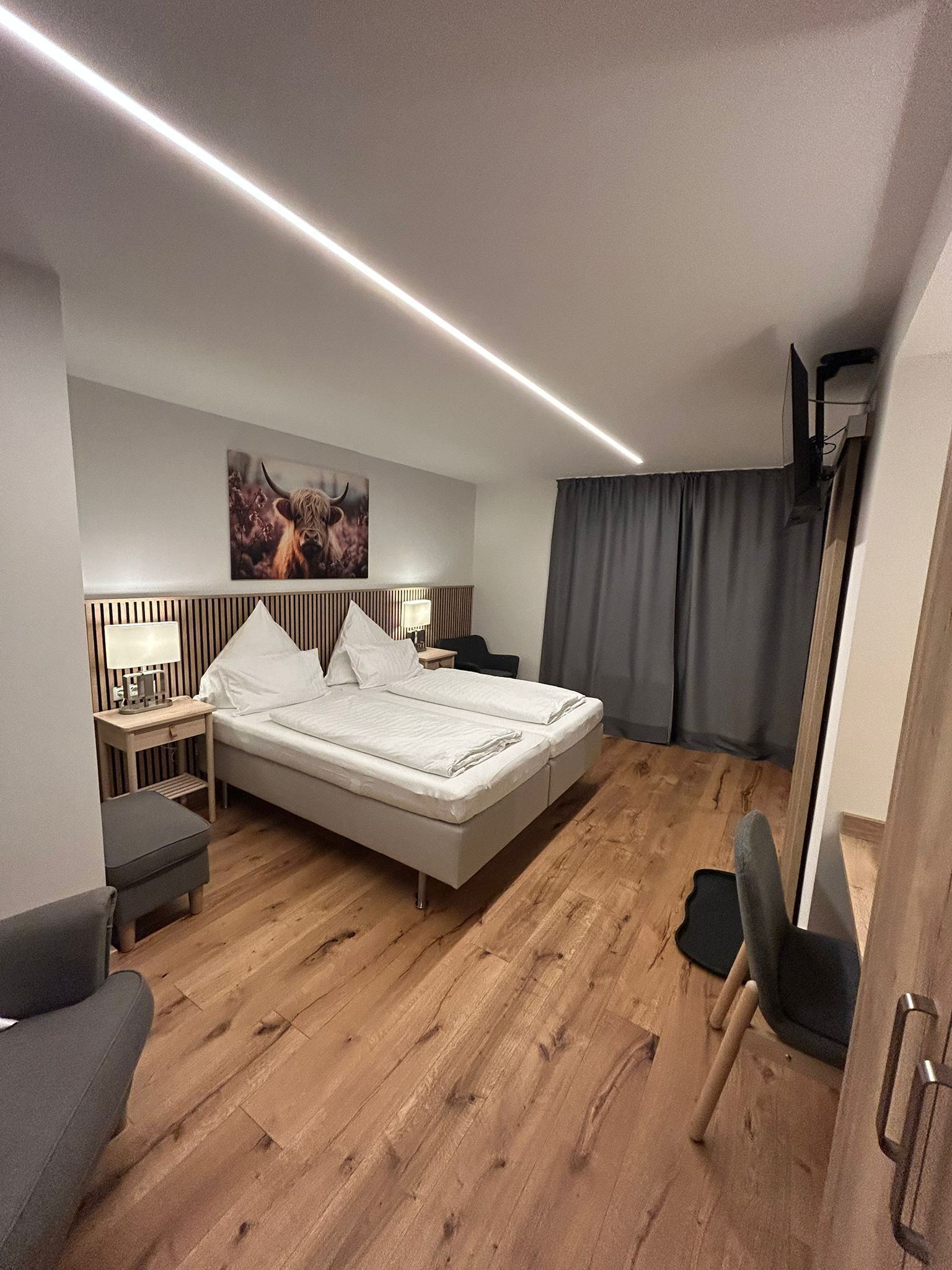 Una habitación de hotel moderna con una cama grande, mesitas de noche, un escritorio, una silla y un televisor montado.