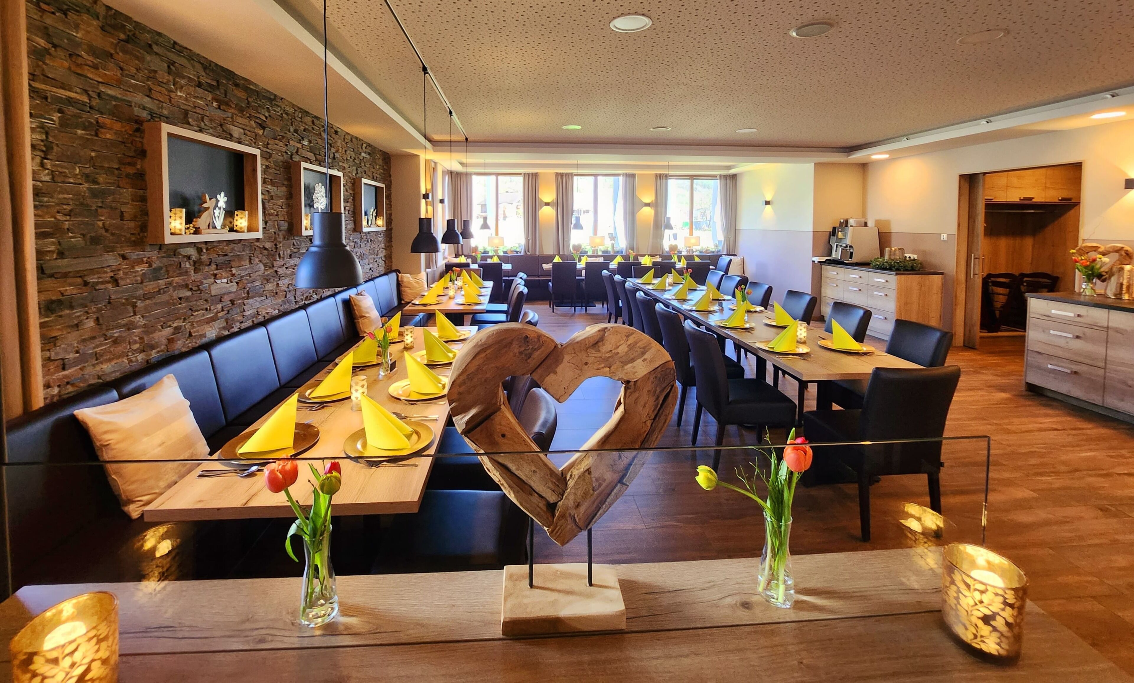 A restaurant with long tables, black chairs, and a stone wall.