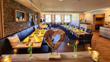 A restaurant with long tables, black chairs, and a stone wall.
