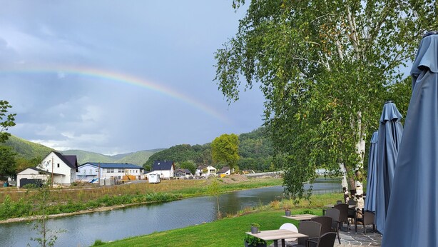 A riverside patio with outdoor seating, a view of a river, and houses in the background.