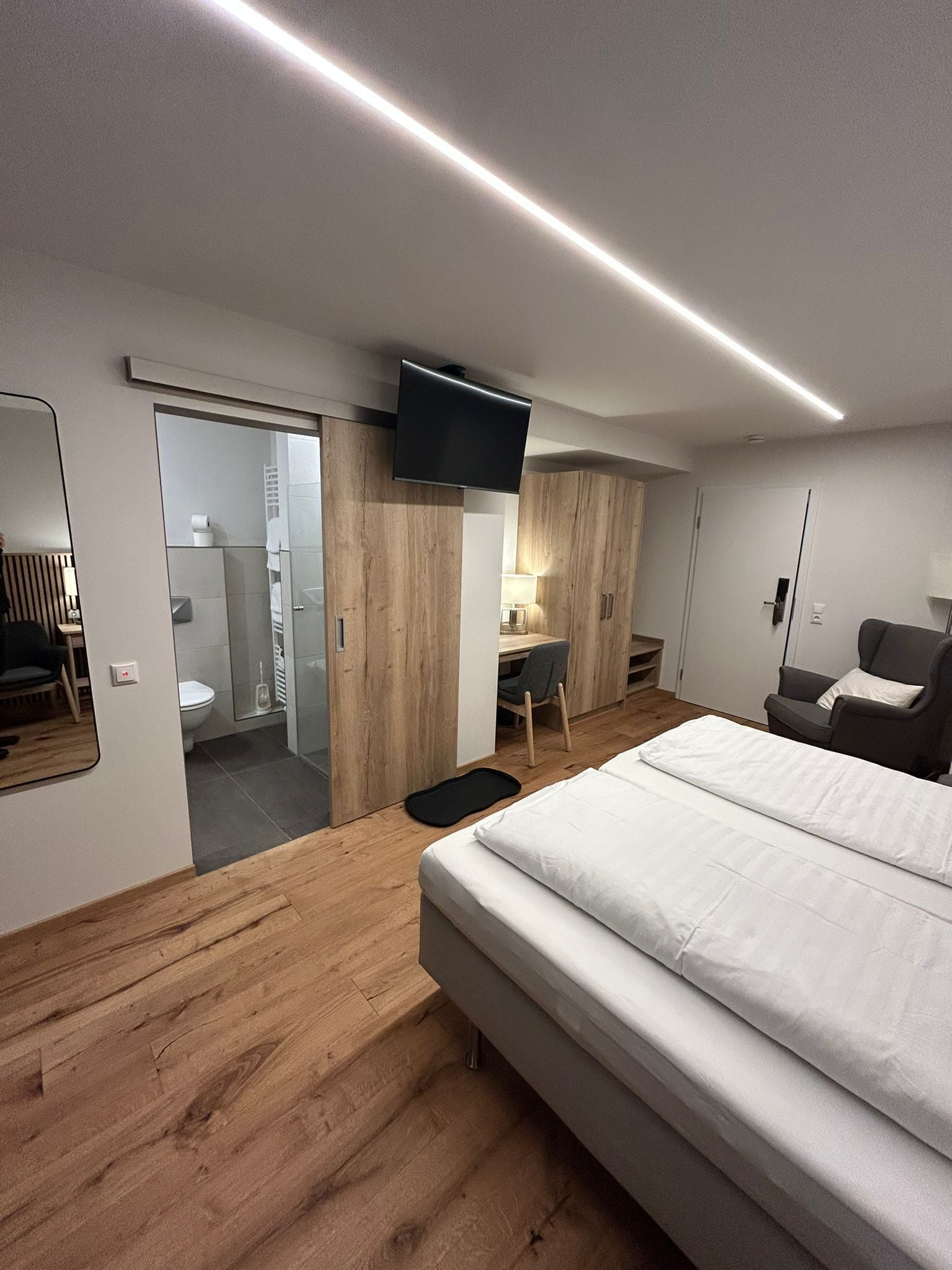 A modern hotel room with a large bed, a desk, a flat-screen TV, and a walk-in closet.