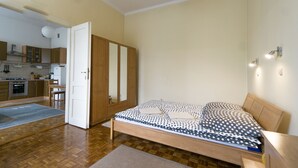 Ein Schlafzimmer mit Bett, Holzschrank und einer kleinen Küchenzeile mit Schränken und Herd.