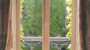 A room with a large window, a wooden chair, and a view of greenery outside. - CHATEAU DE LA VERNEDE (Saint-Rémy-de-Chargnat)