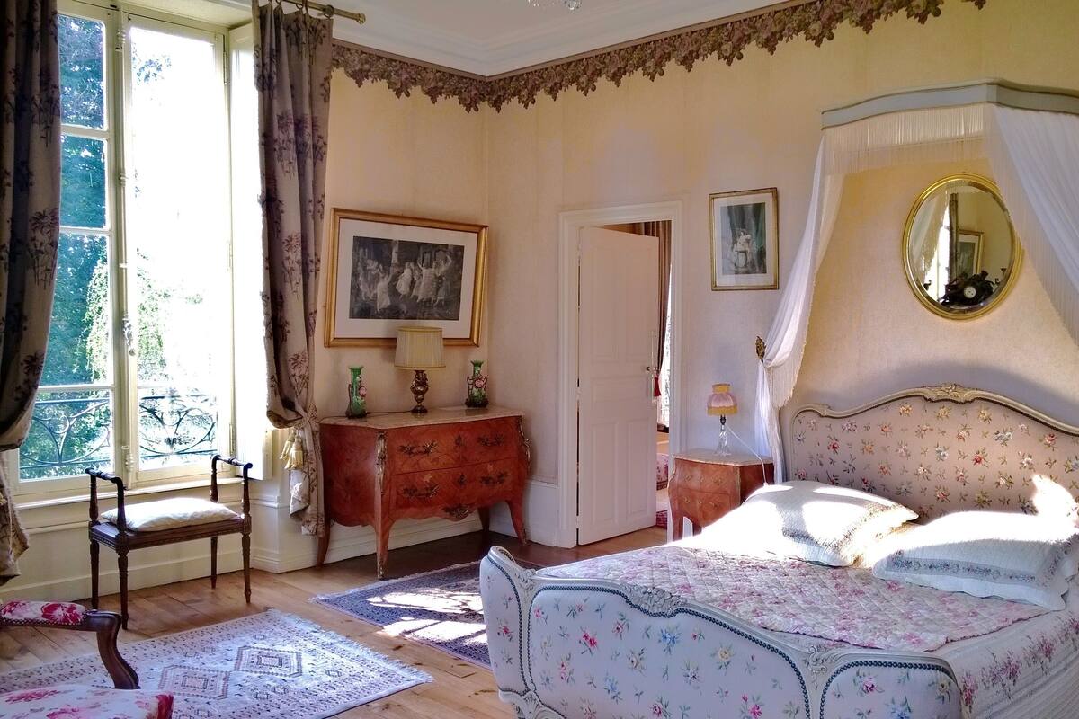 A bedroom with a four-poster bed, a dresser, a mirror, and a window with curtains.