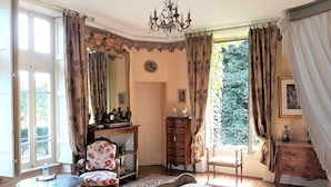 A bedroom with a large bed, a chair, a dresser, a small table, and a fireplace. - CHATEAU DE LA VERNEDE (Saint-Rémy-de-Chargnat)
