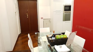 A small kitchen with white cabinets, a microwave, and an oven. There is a glass table with a bottle, bread, and a basket of fruit. - S. PETER - BIG APARTMENT IN FRONT OF DOME WITH VIEW (Roma)