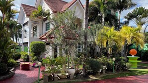A two-story building with a red-tiled roof, surrounded by lush greenery and palm trees. - Sir Nico Guesthouse and Resort (Plaridel)