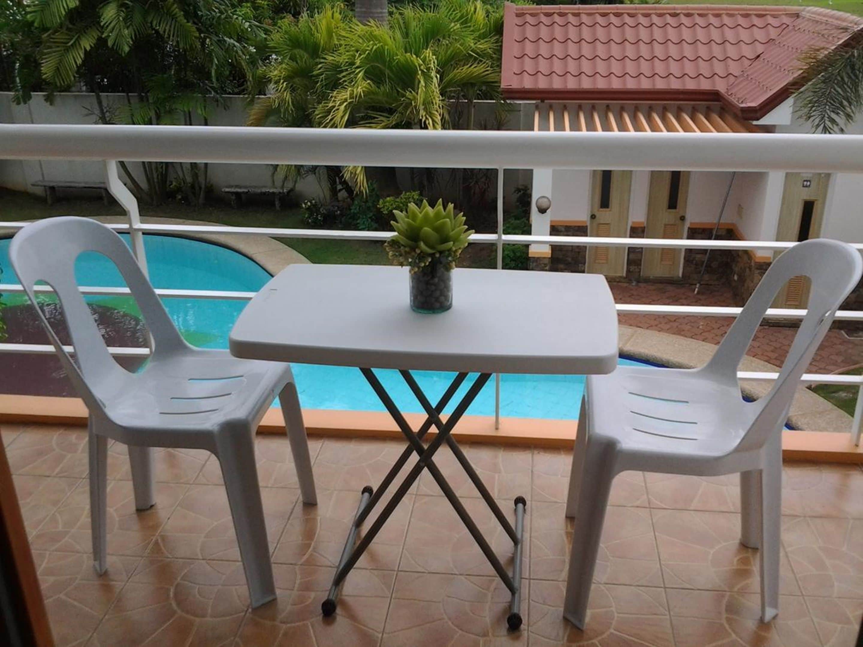 A balcony with a pool, two white plastic chairs, and a small table with a potted plant.
