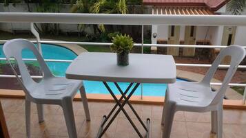 A balcony with a pool, two white plastic chairs, and a small table with a potted plant.
