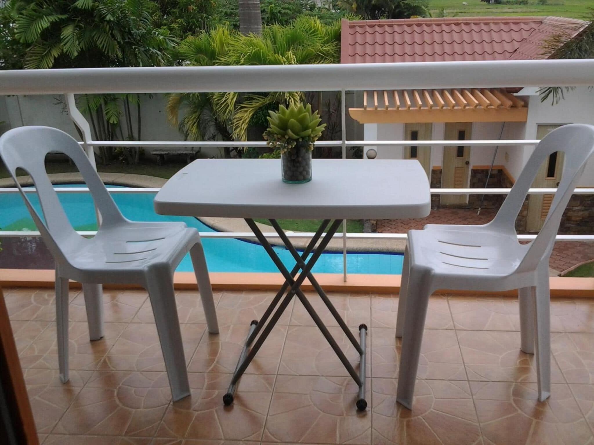 Un balcón con piscina, dos sillas de plástico blancas y una pequeña mesa con una planta en maceta.