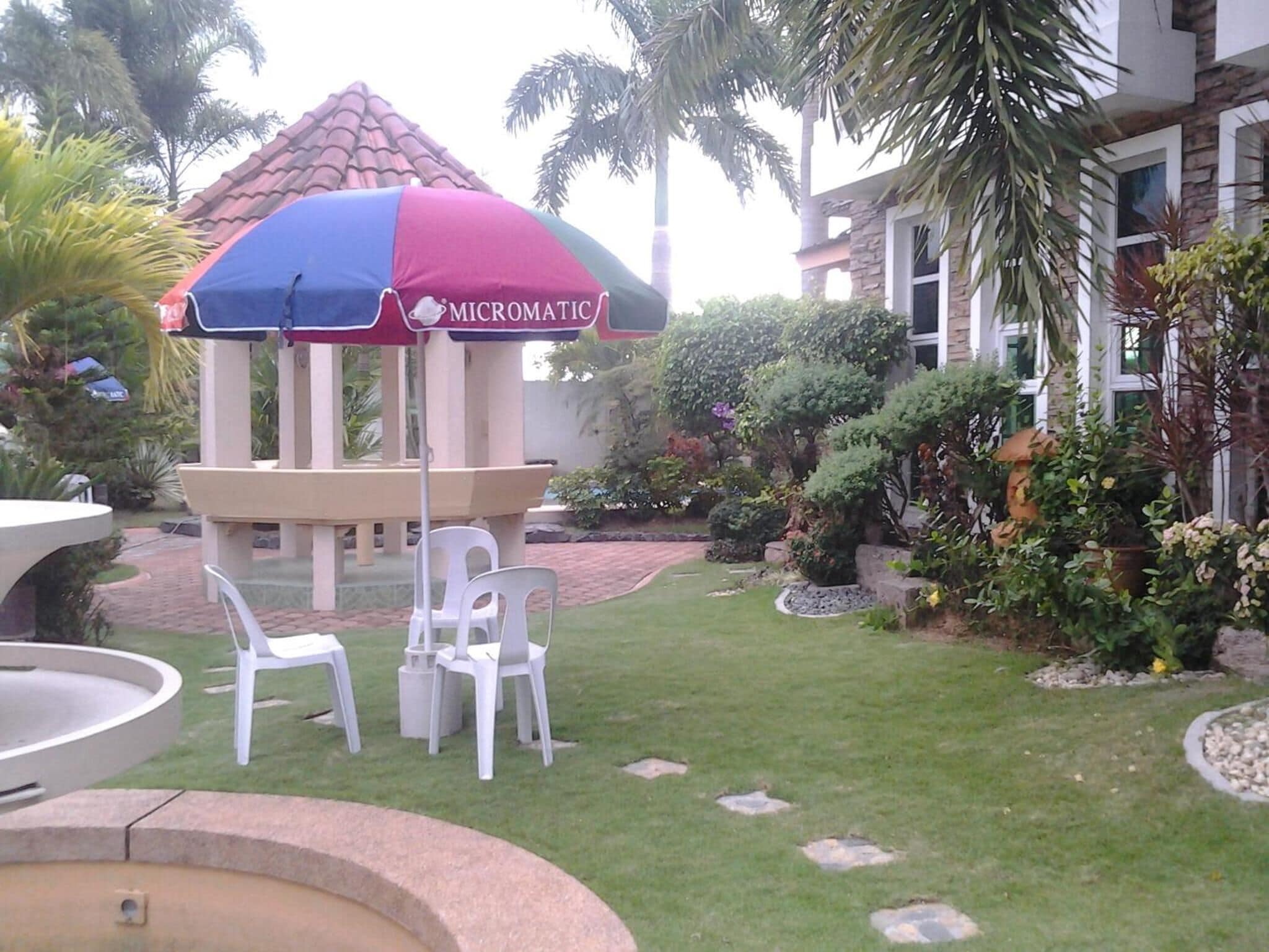 A gazebo with a Micromatic umbrella, surrounded by white plastic chairs and a small fountain.