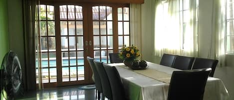 A dining area with a table set for four, a fan, and a view of a swimming pool through glass doors.
