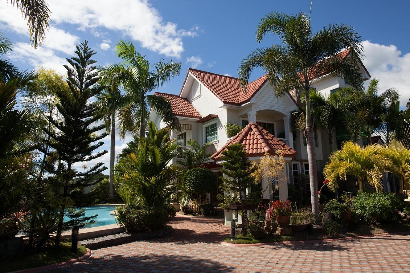 A large house with a swimming pool, surrounded by palm trees and a garden.
