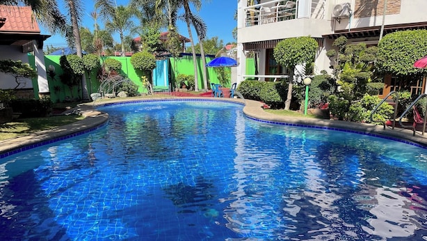 A swimming pool with a tiled edge, surrounded by greenery and a building with a balcony. - Sir Nico Guesthouse and Resort (Plaridel)