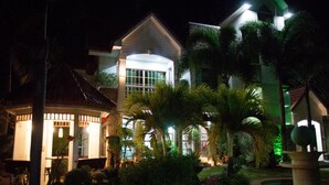 A modern building with a large glass window, surrounded by lush greenery and palm trees. - Sir Nico Guesthouse and Resort (Plaridel)