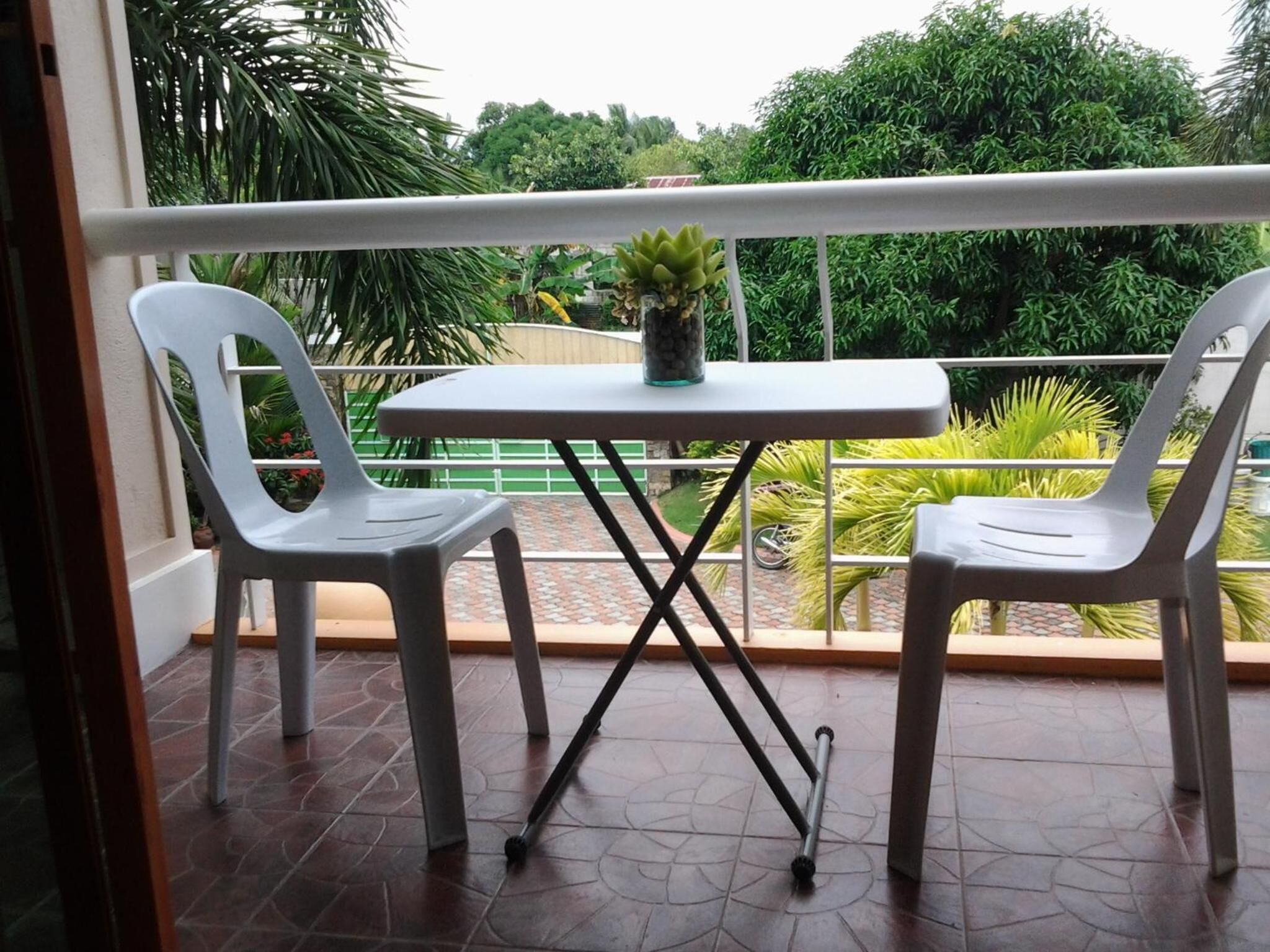 Uma varanda com duas cadeiras de plástico branco e uma pequena mesa, com um vaso de planta sobre a mesa.