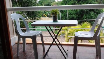 Uma varanda com duas cadeiras de plástico branco e uma pequena mesa, com um vaso de planta sobre a mesa.