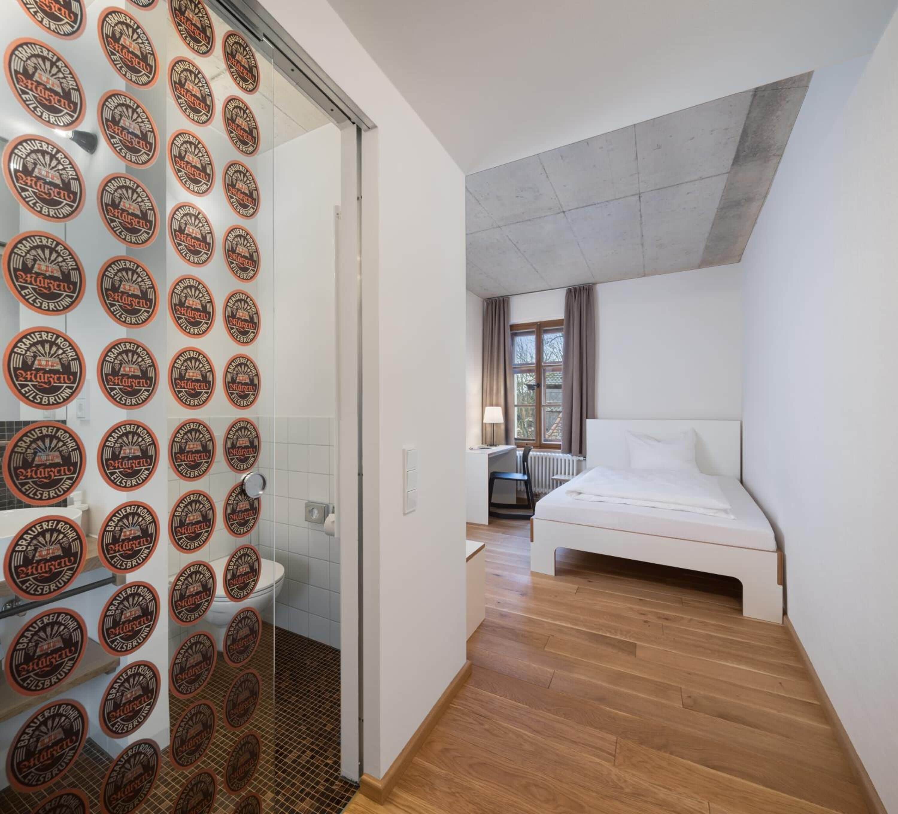 A modern bedroom with a large bed, a desk, and a bathroom with a shower.