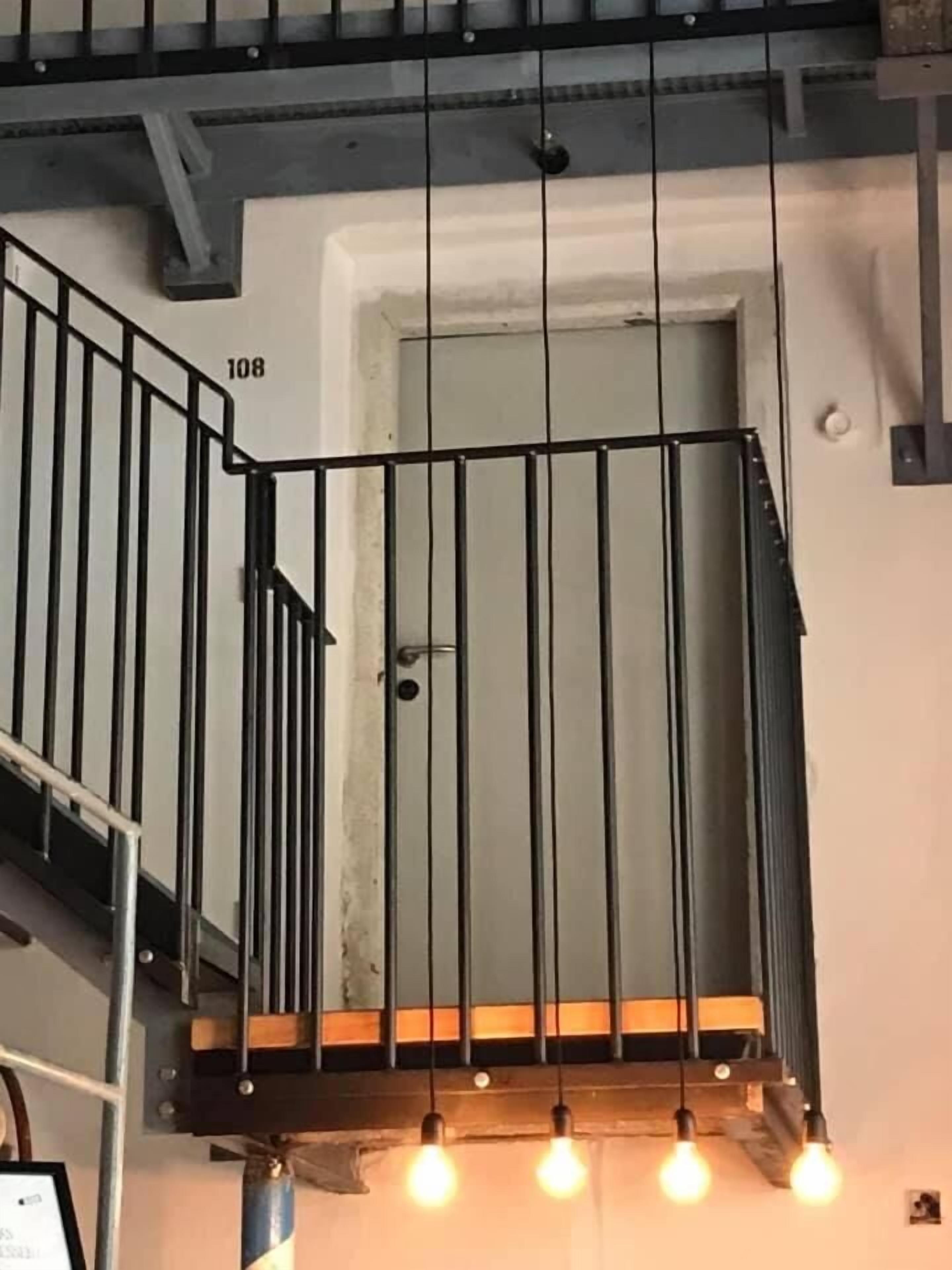 A staircase with a metal railing, a door labeled "108", and three hanging light bulbs.
