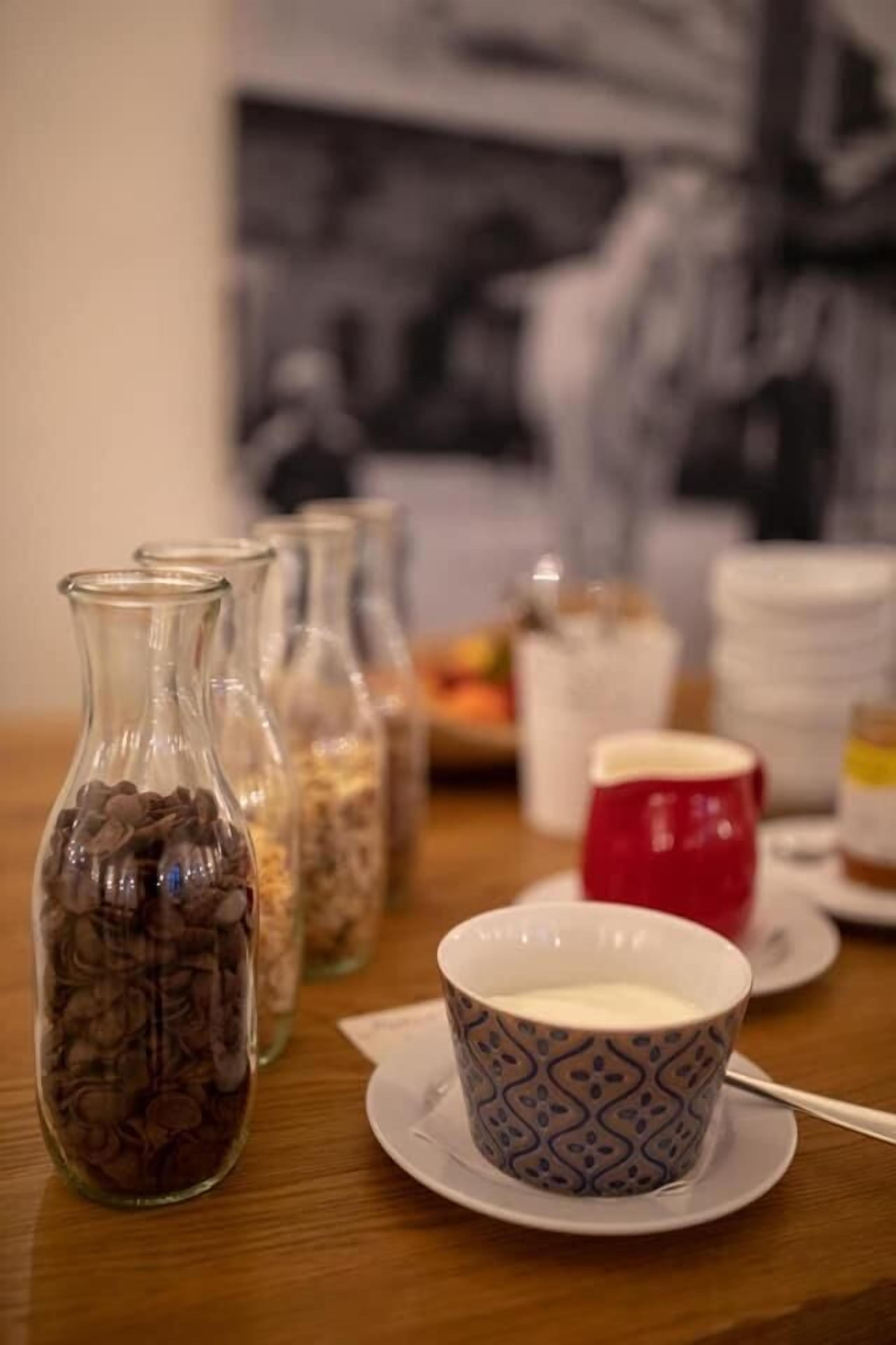 A dining table with a coffee cup, a red mug, and several glass jars containing different items.