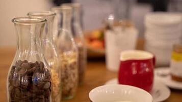 A dining table with a coffee cup, a red mug, and several glass jars containing different items.
