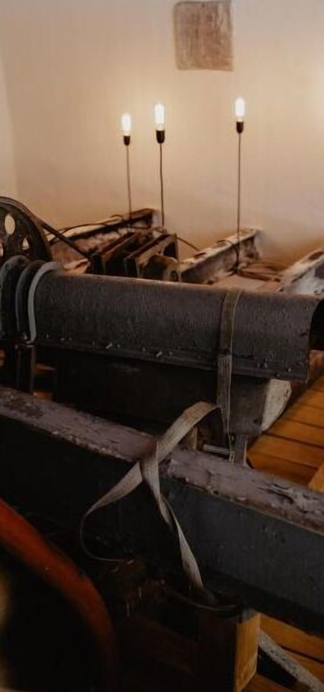 An antique printing press with two light bulbs mounted on the wall above it.