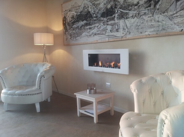 A living room with a white armchair, a small white table, a floor lamp, and a fireplace.