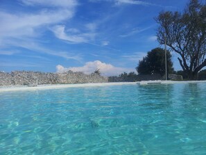 A clear blue pool surrounded by a stone wall and a tree. - Falcon Home Resort (Lizzanello)