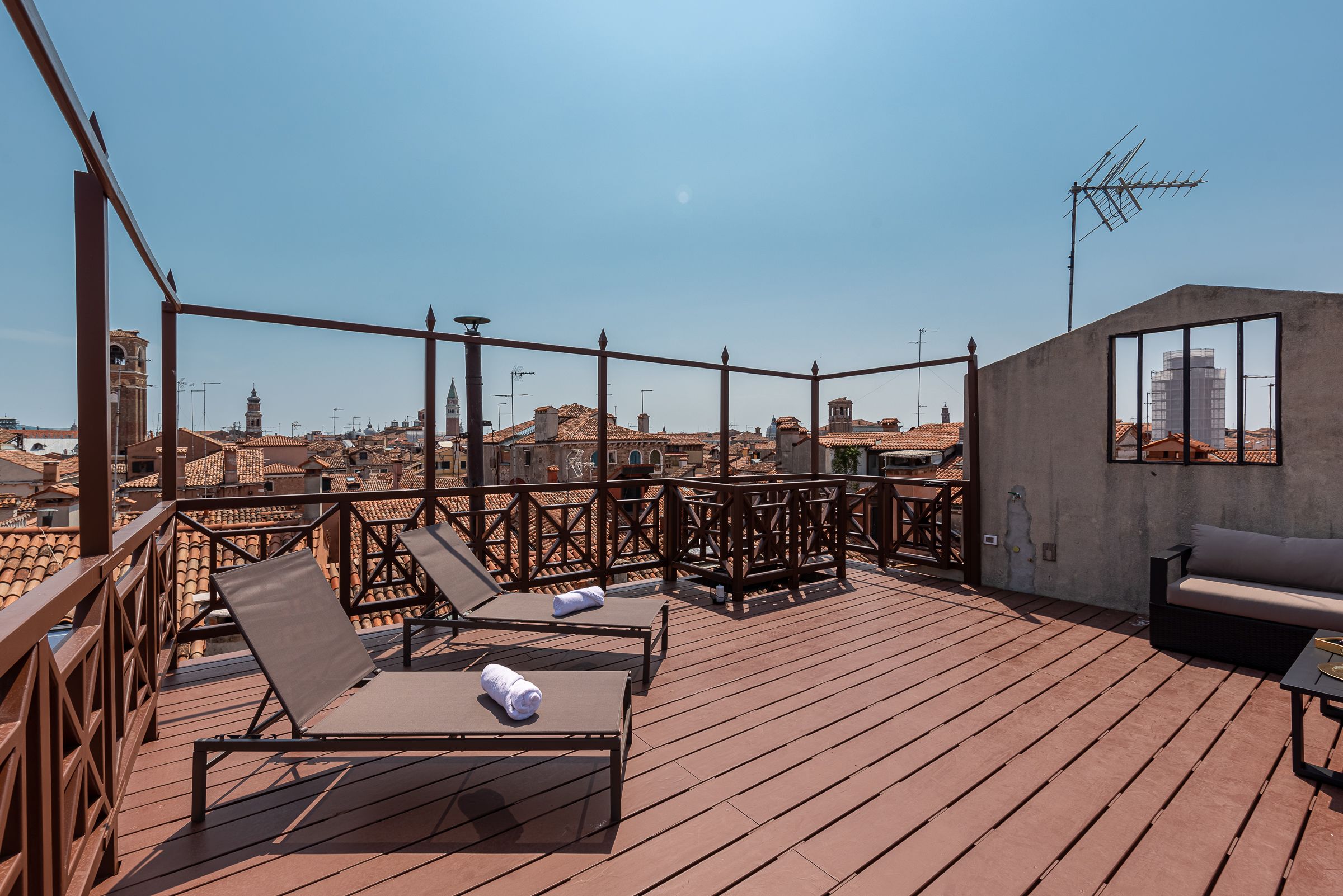 Una terraza en la azotea con piso de madera, sillones de descanso y un sofá.