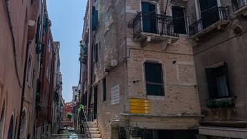 Une rue étroite, bordée de bâtiments des deux côtés, avec un canal d’eau visible et un escalier menant à un immeuble.