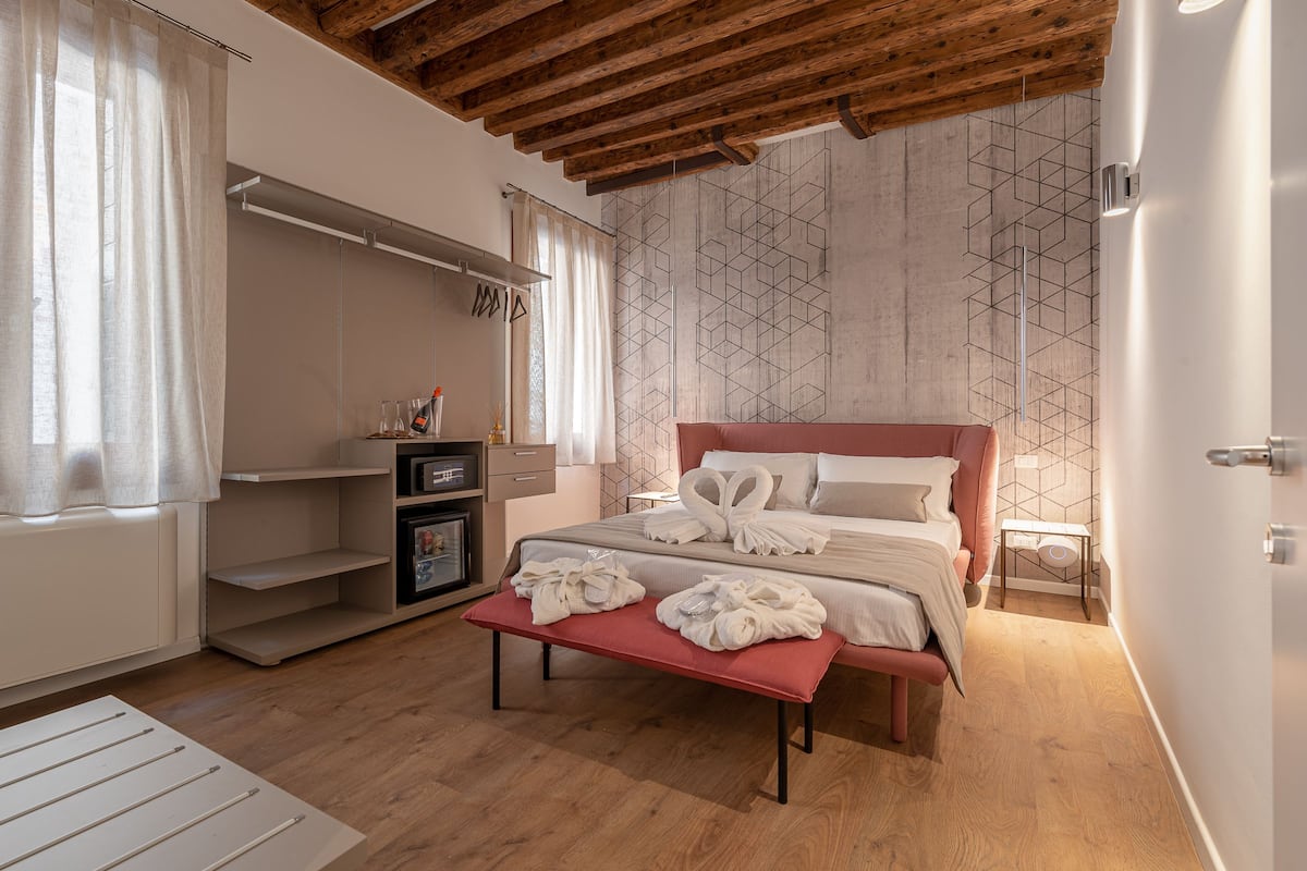 A bedroom with a wooden ceiling, a bed with towels, a bench, a wardrobe, and a wall with a geometric pattern.