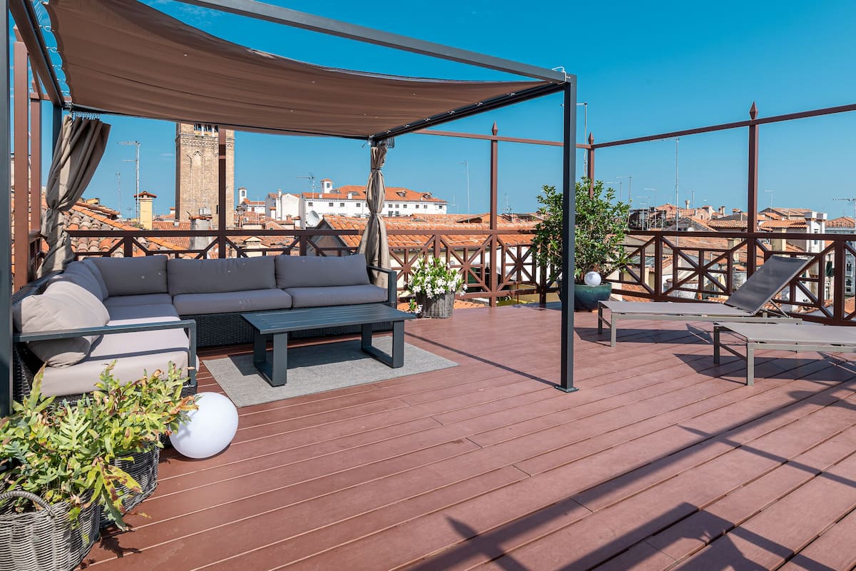 A rooftop terrace with a sofa, lounge chairs, and potted plants.