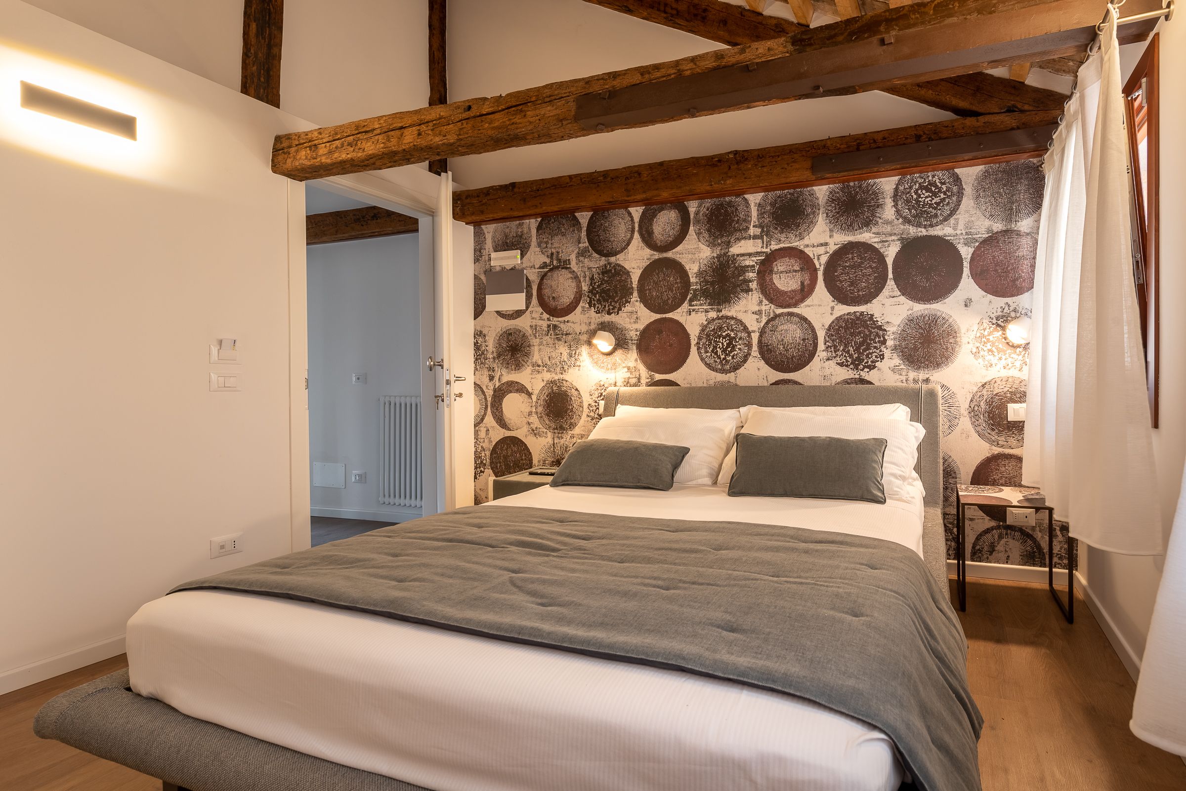 Une chambre à coucher avec un lit, des poutres en bois, un mur à motifs et un radiateur.