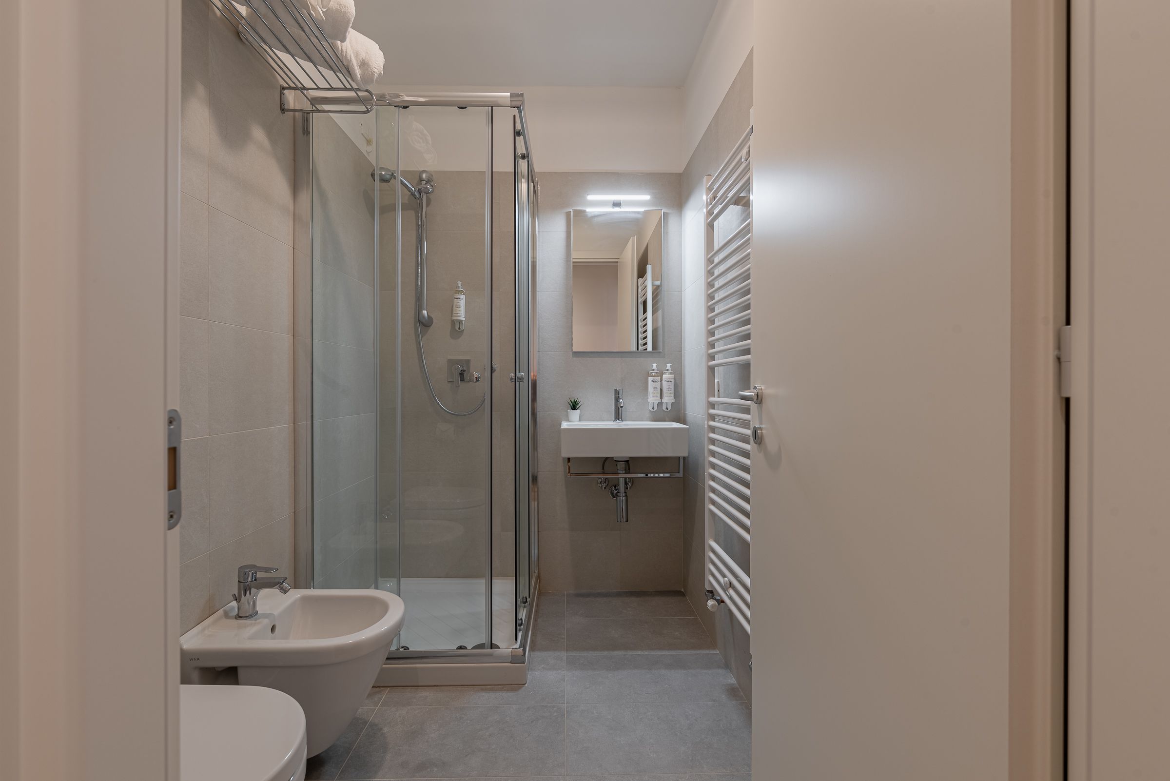 A modern bathroom with a glass-enclosed shower, a pedestal sink, and a toilet.