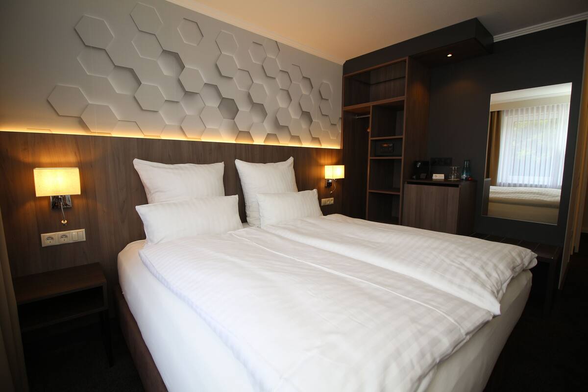 A hotel room with a large bed, two bedside lamps, a wooden headboard, and a geometric wall design.