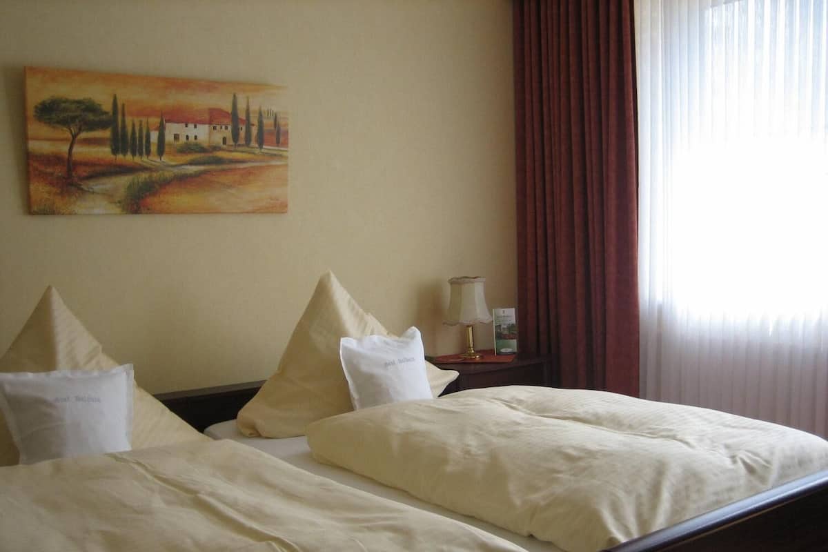 A hotel room with a bed, pillows, a nightstand, a lamp, and a painting on the wall.