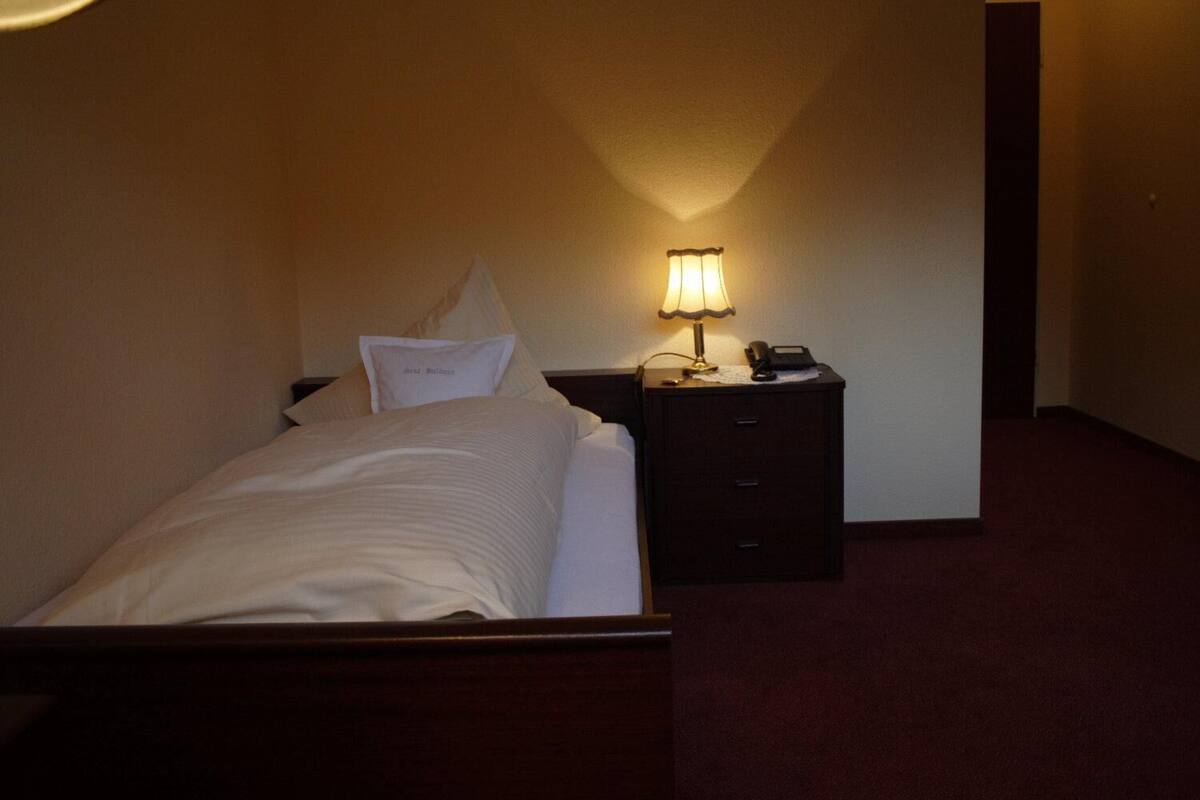 A neatly made bed with a pillow and a bedside table with a lamp and a phone.