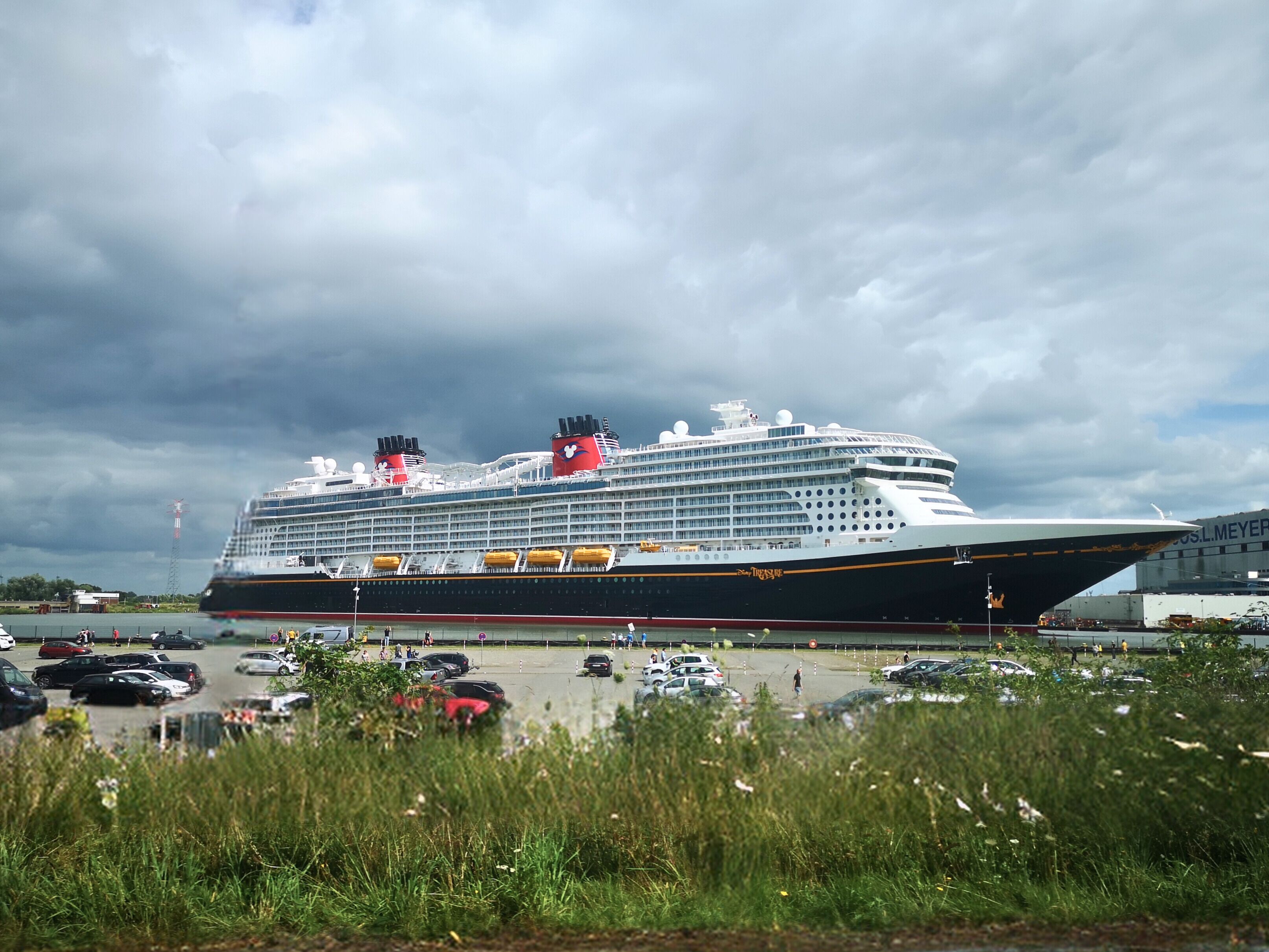 A large cruise ship docked at a port with a cloudy sky in the background.