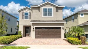 A two-story house with a garage, a front door, and a small porch. - Delightful Home with Private Pool Oasis in Encore (Kissimmee)