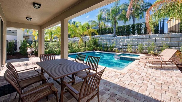 A covered patio with a pool, outdoor furniture, and a stone wall. - Delightful Home with Private Pool Oasis in Encore (Kissimmee)