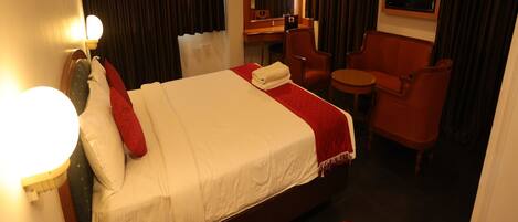A hotel room with a bed, a desk, a chair, a TV, and a red carpet.