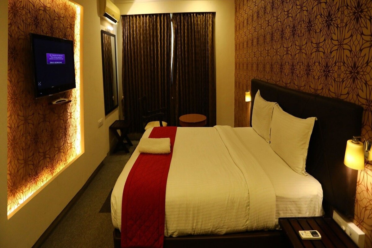 A hotel room with a bed, a television mounted on the wall, a ceiling fan, and a patterned wallpaper.