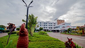 A hotel with a modern design, featuring a central courtyard with a statue, lush green grass, and a variety of plants. - DFRONT Golden Palace (Namakkal)