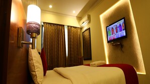 A hotel room with a bed, a television mounted on the wall, a ceiling fan, and a window with curtains. - DFRONT Golden Palace (Namakkal)