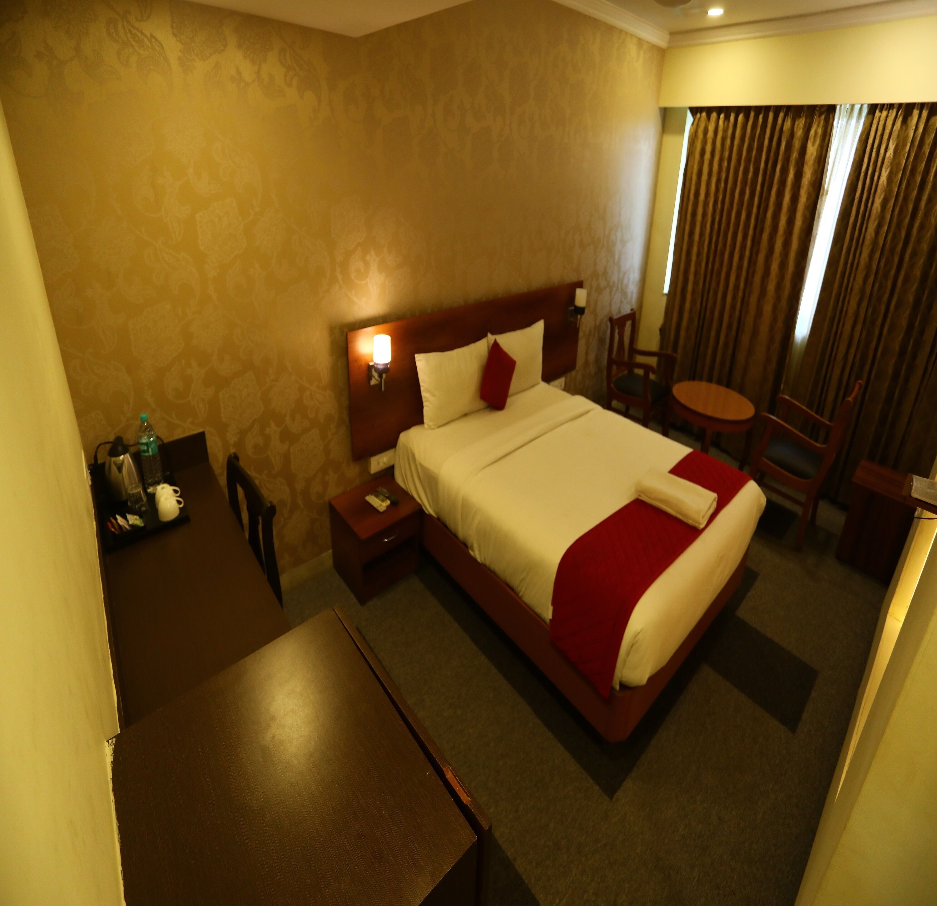 A hotel room with a large bed, a bedside table, a desk, and a chair.