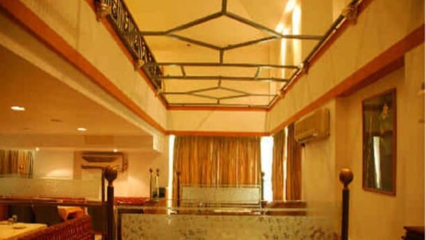 A hotel lobby with a high ceiling, a central seating area, and a large window with curtains. - DFRONT Golden Palace (Namakkal)