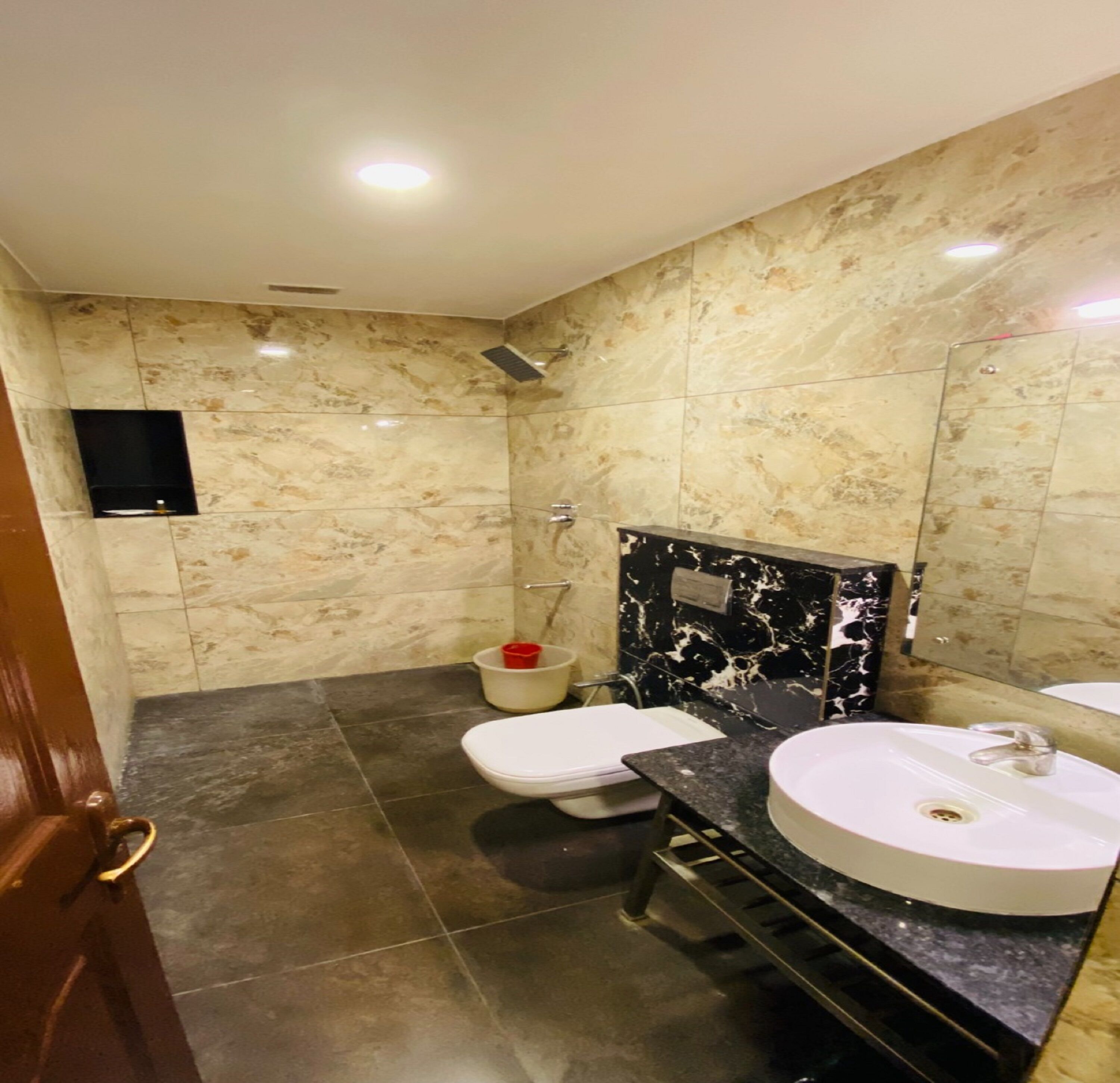A bathroom with a marble wall, a black marble sink, a white toilet, and a shower.