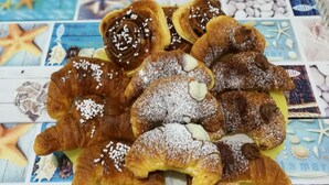 A variety of pastries on a green plate, including croissants and cinnamon rolls, with a nautical-themed tablecloth in the background. - B&B Laura e Chiara (Trapani)